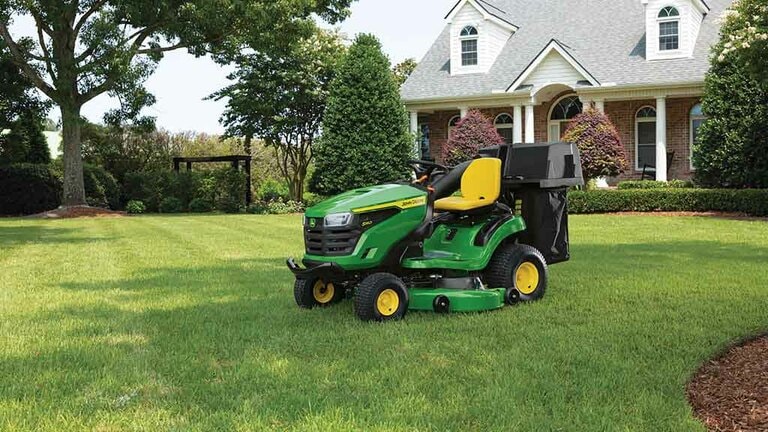 A green riding mower sitting on a well-kept lawn with a bagging attachment. (7th thumbnail)