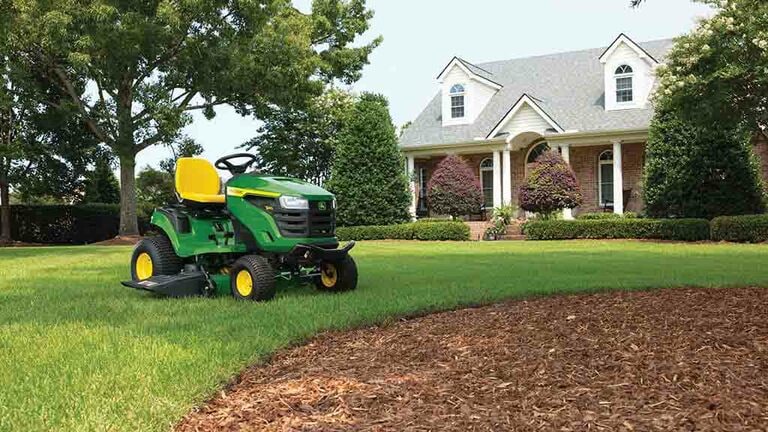 A rounded patch of mulch with a green riding mower next to it sitting on a grassy lawn. (9th thumbnail)