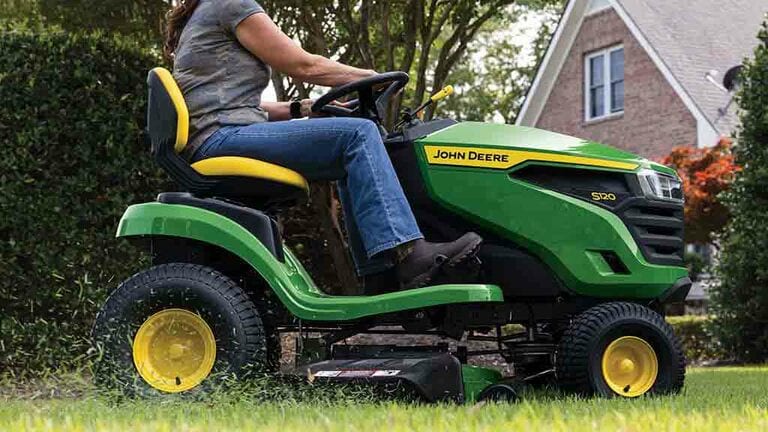 A close-up right side view of a green riding mower with grass clippings coming out the side of the deck. (7th thumbnail)