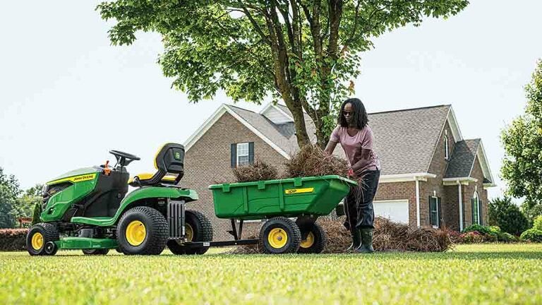 A person loading a green cart attached to the back of a green riding mower. (8th thumbnail)