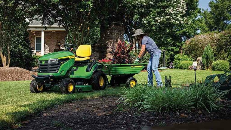Plants being handled in a green cart attached to the back of a green riding mower. (5th thumbnail)