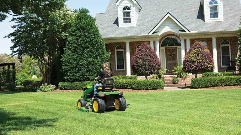 A person driving back-and-forth on a grassy lawn with a green riding mower. (9th thumbnail)