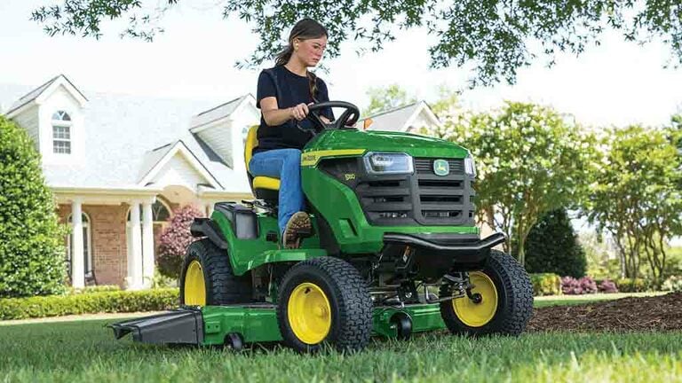 A person rounding the edge of a patch of mulch with a green riding mower. (8th thumbnail)