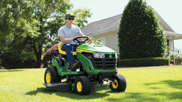 Close-up of a person driving a green riding mower over a flat even lawn. (6th thumbnail)