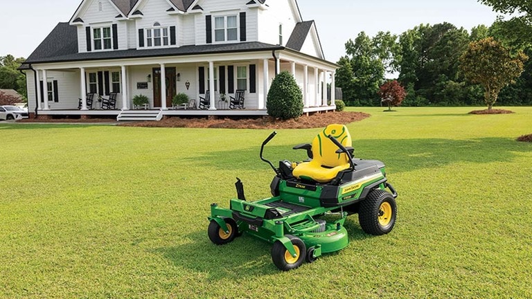 A green zero-turn mower sitting in front of a residence on a well-kept lawn. (5th thumbnail)