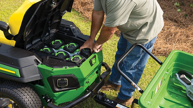 A person reaching into the battery compartment of an electric zero-turn mower and pulling out a battery. (6th thumbnail)