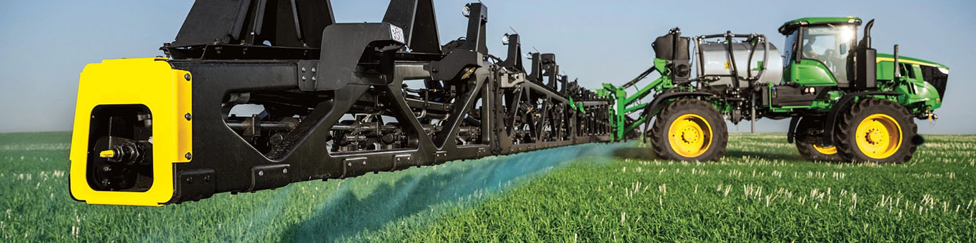 Photograph shot from the side showing a See&SprayTM-equiooed John Deere Sprayer in a field with its boom fully extended.