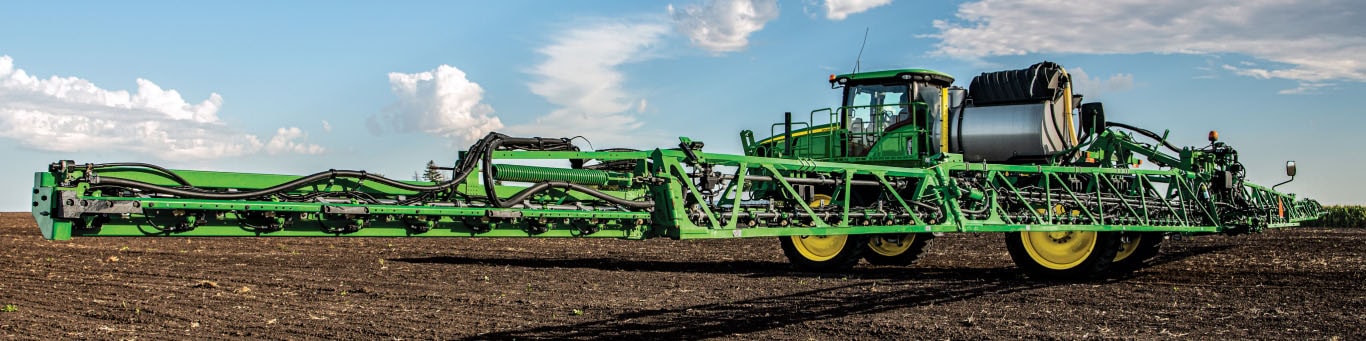 Ground level photograph of a sprayer in a fallow field – with booms fully extended, looking from the right rear.