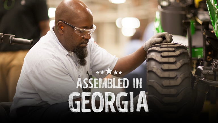 An assembler with eye and ear protection attaches a tire onto a riding lawn mower. (10th thumbnail)