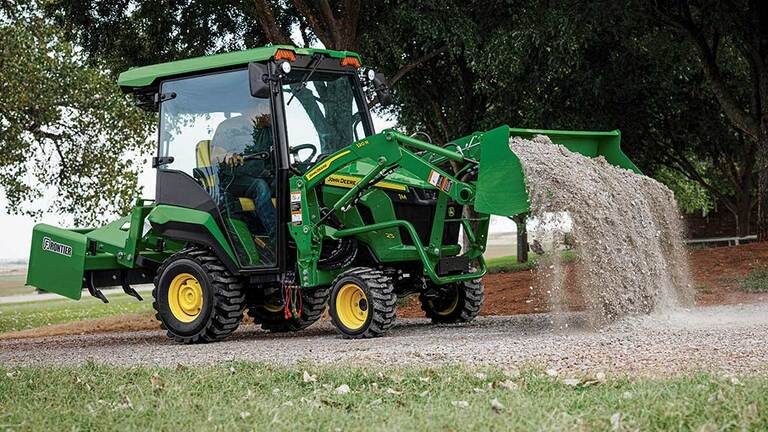 A green compact tractor with a cab, land plane, and loader dumping gravel on a gravel road. (6th thumbnail)