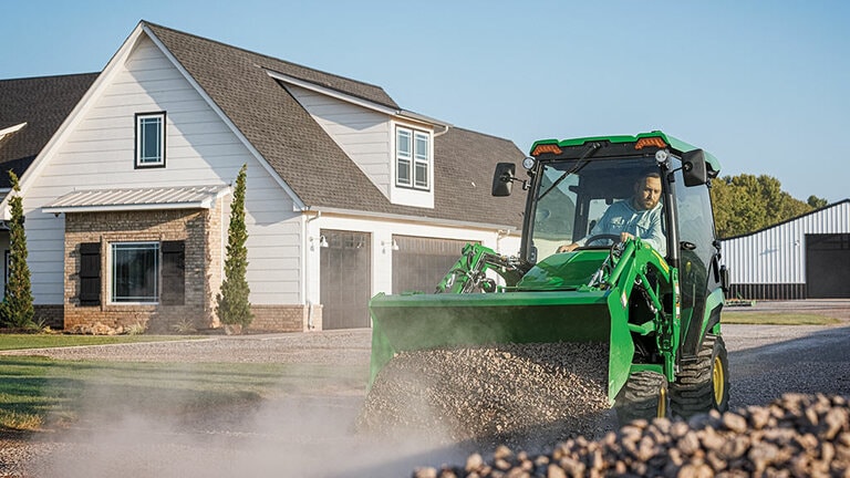 A cabbed green compact tractor using a loader to push gravel down a gravel road. (4th thumbnail)