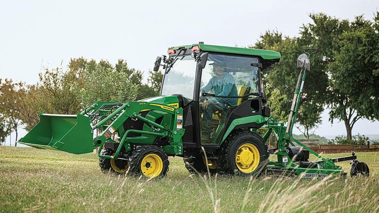 A cabbed green compact tractor with a loader pulls a rotary cutter over some grass. (4th thumbnail)
