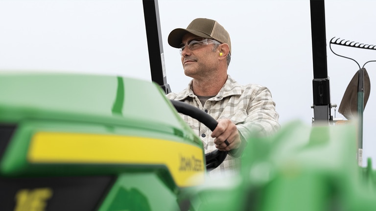 Close up of a person smiling atop an out-of-focus green compact tractor. (4th thumbnail)