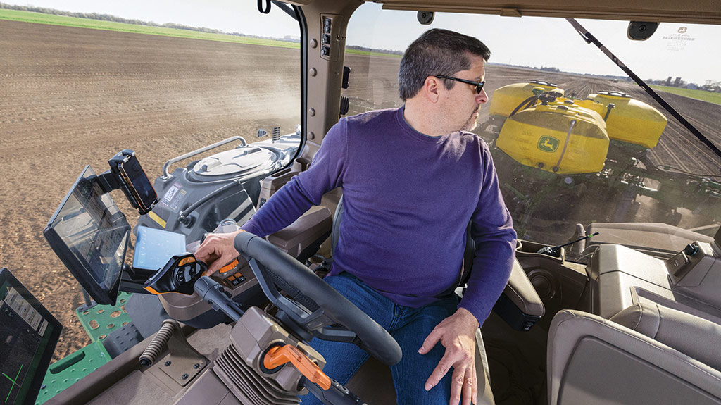 Operator in cab swiveled in his seat looking back at a planter while operating a high-horsepower 8 Series Tractor. Operator in cab swiveled in his seat looking back at a planter while operating a high-horsepower 8 Series Tractor.
