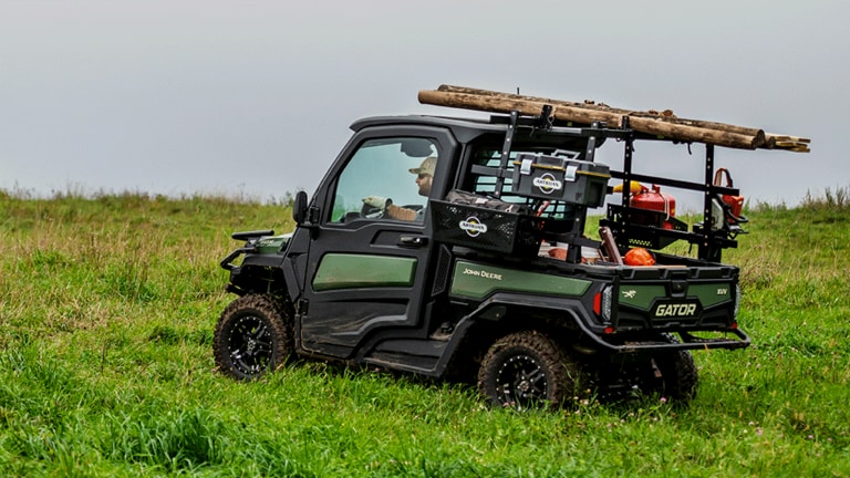 A HVAC cabbed olive-green Gator carries a load of timber on a rack along with a cargo box full of tools and supplies. (12th thumbnail)