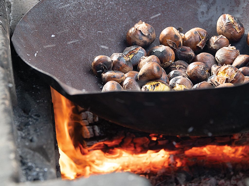  closeup of chestnuts in cast iron pan roasting over open fire