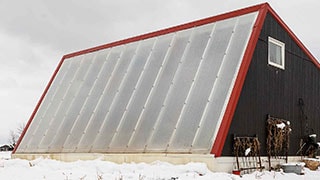 black greenhouse with red trim and translucent white windows surrounded by snow