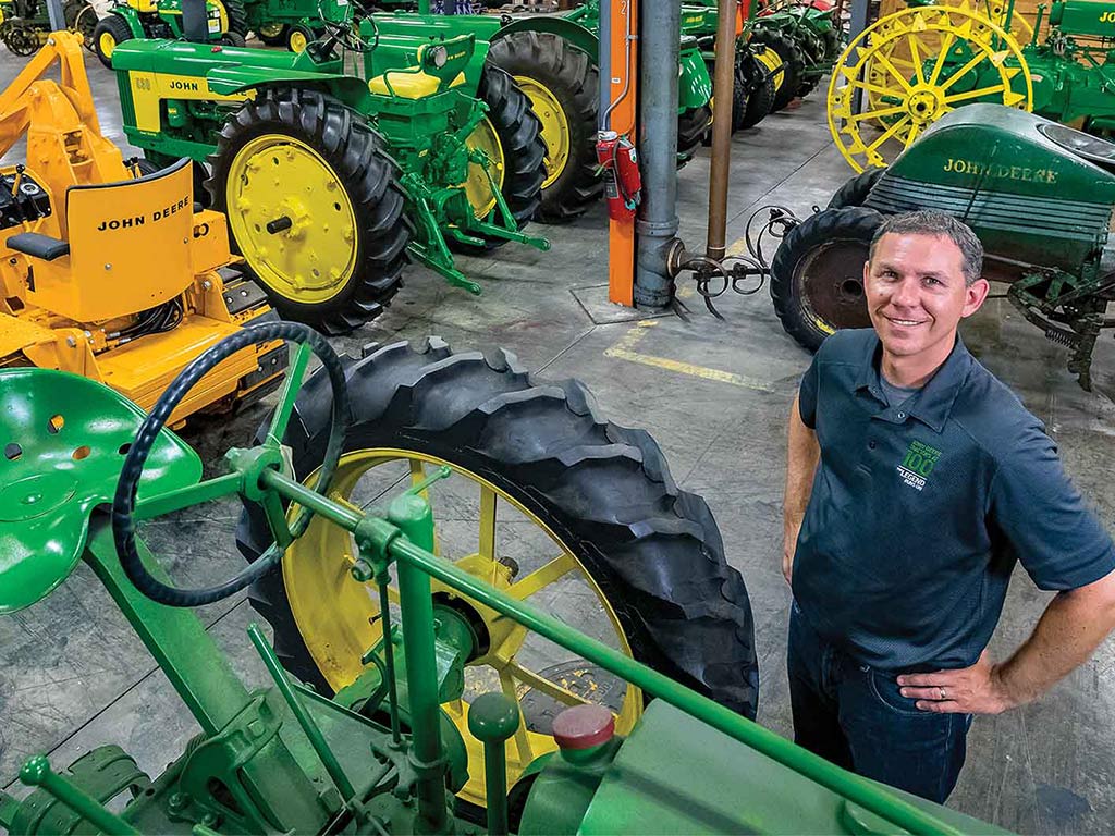 Neil Dahlstrom smiling among vintage John Deere equipment with his hands on his hips