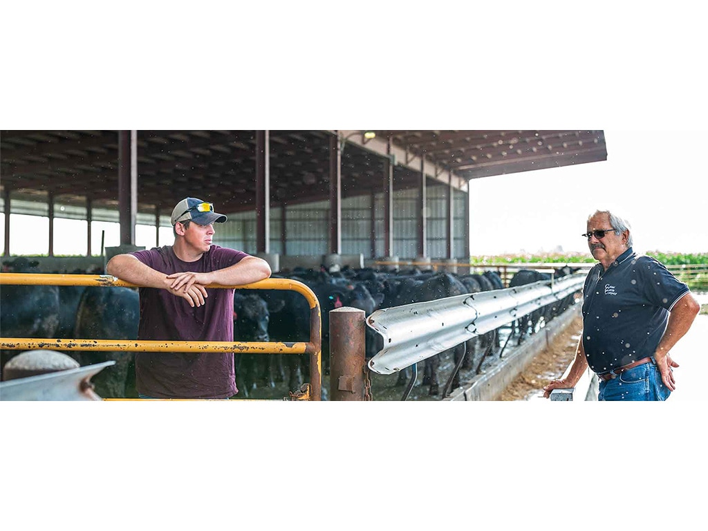 two cattle farmers standing near a covered feedlot