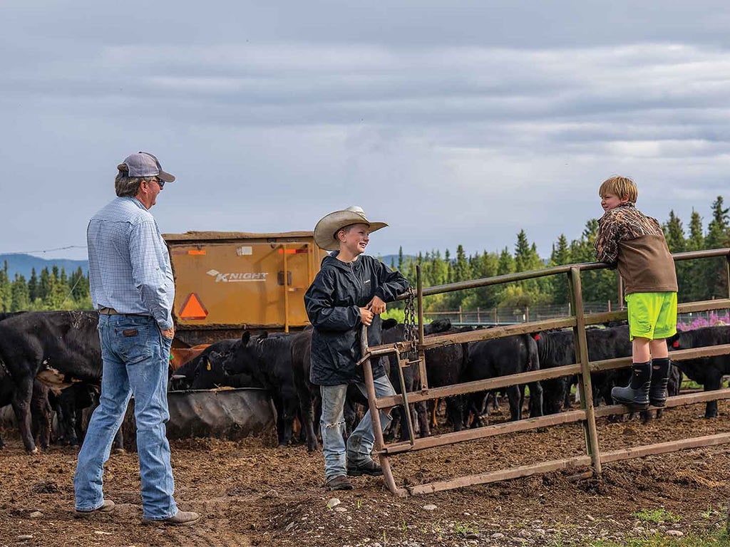 three farmers standing and sitting on cattle gate