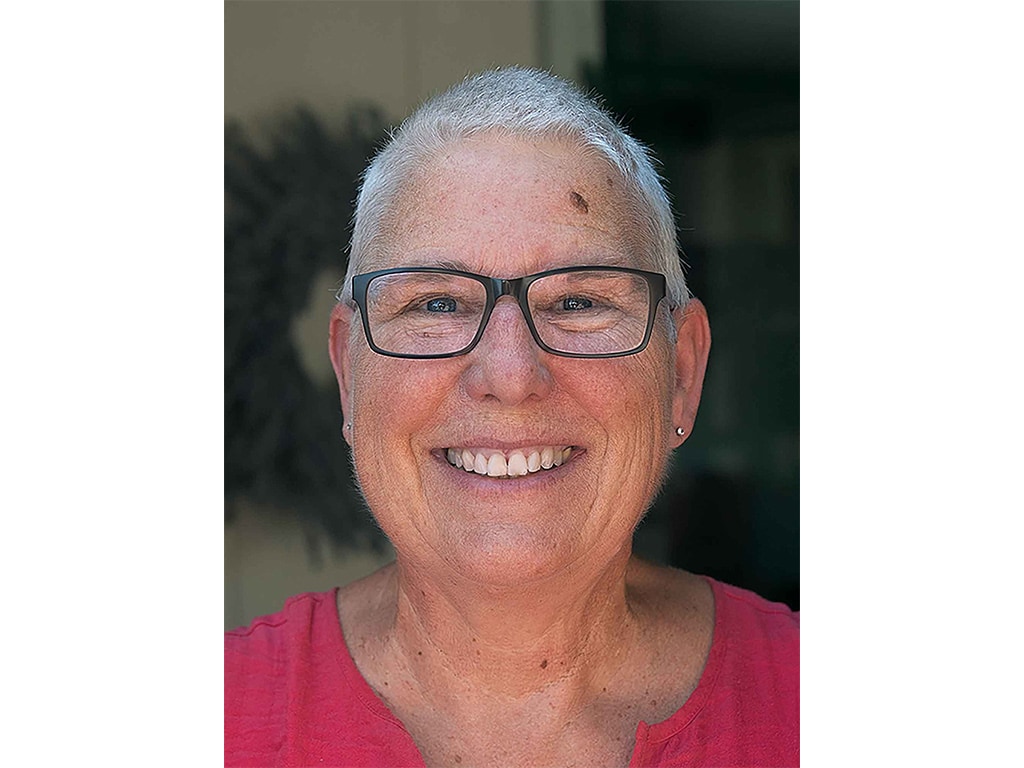 closeup of smiling person with short white hair, wearing black-rimmed eyeglasses and a red shirt