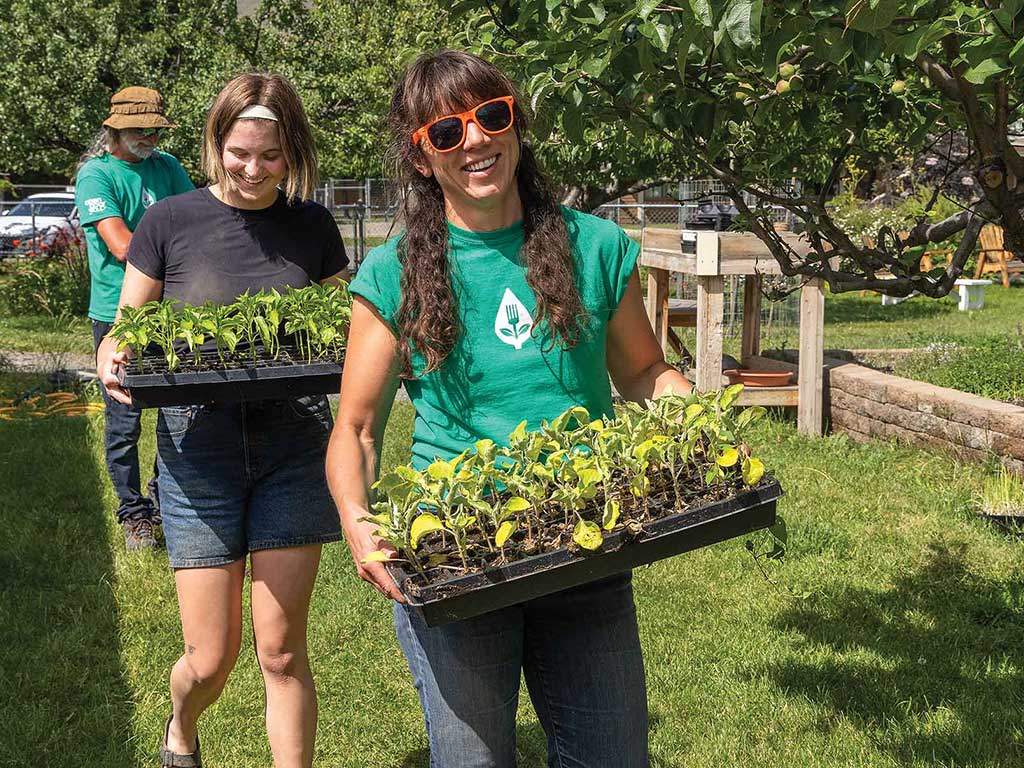 Three smiling volunteers carrying flats of plant seedlings