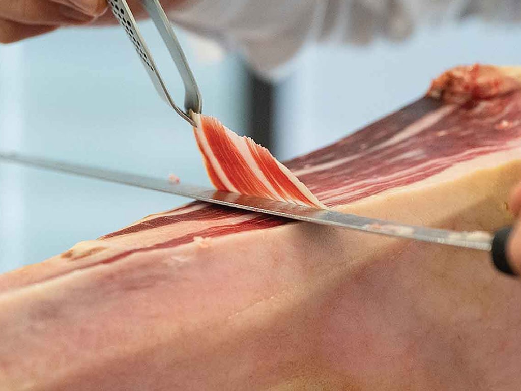 closeup of a knife thinly slicing Spanish ham