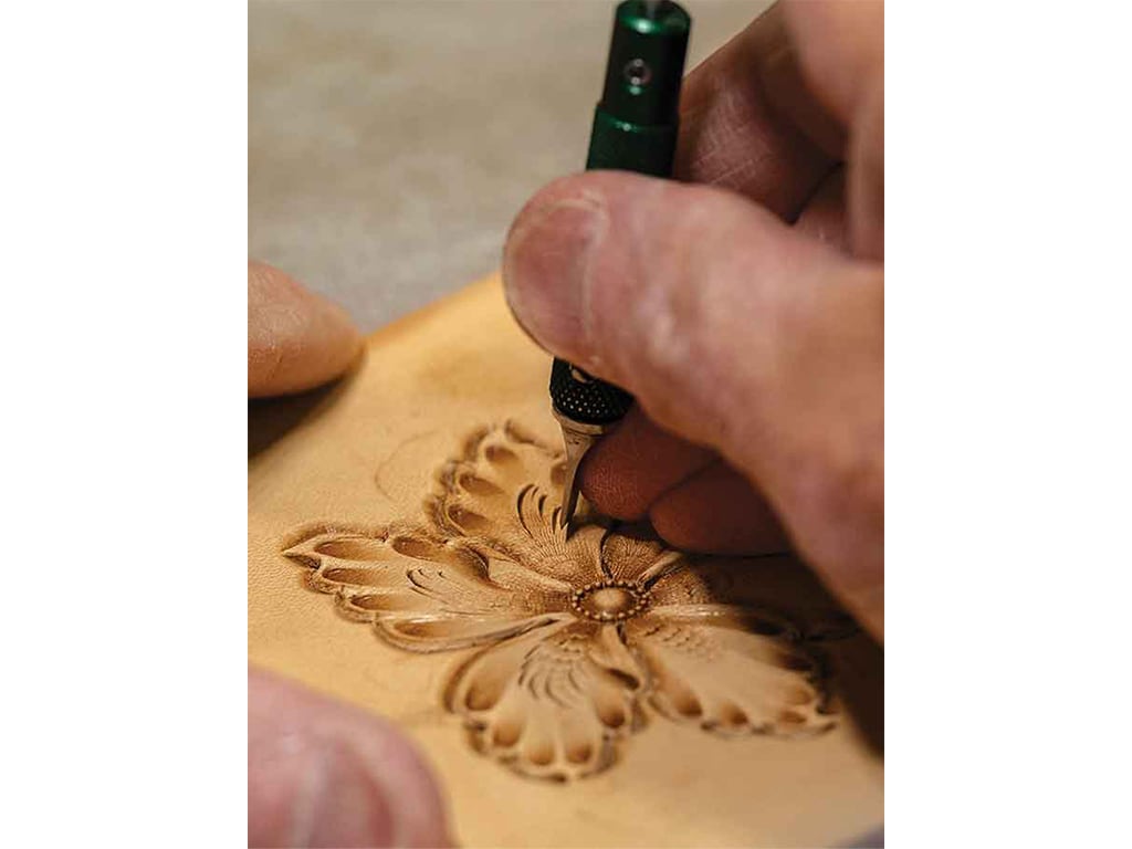 closeup of the craftsman carving a small intricate flower in leather