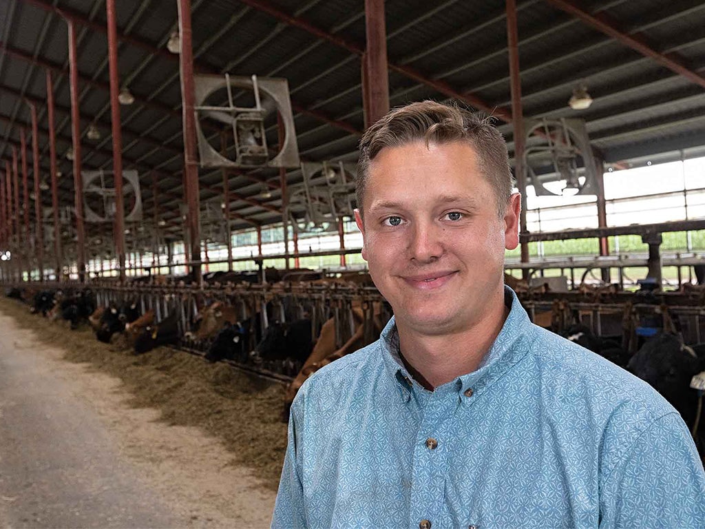 Smiling cattle farmer standing in front of long covered feedlot with fans attached to posts