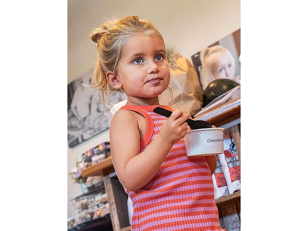 a little girl eating out of a white paper cup with a black plastic spoon