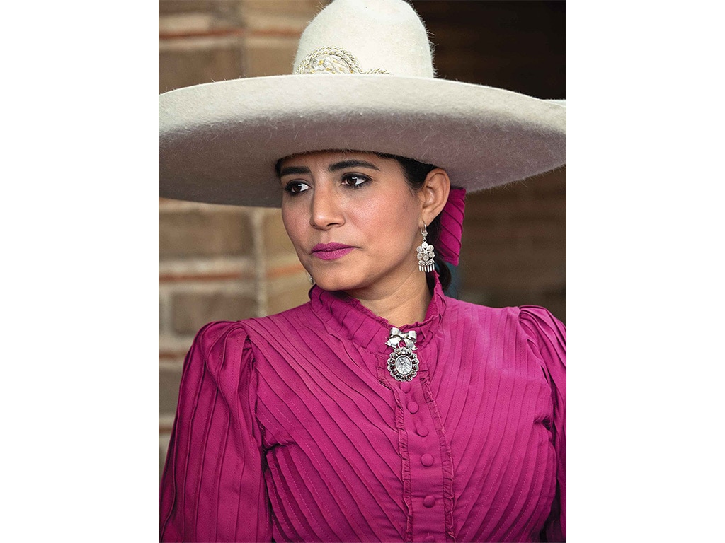 closeup of an escaramuza rider wearing a rich fuchsia coat and bone white wide brimmed hat with a rounded crown