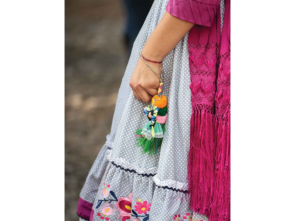 closeup of an escaramuza rider's hand with a good luck ornament dressed in similar clothes to the rider hanging off of their wrist