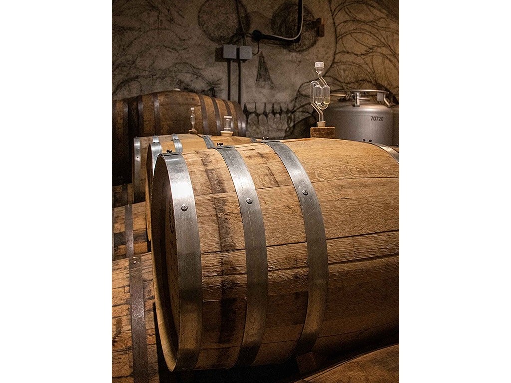 several oak barrels stacked on their sides with a skull drawn on the back wall with steel tanks in front of it