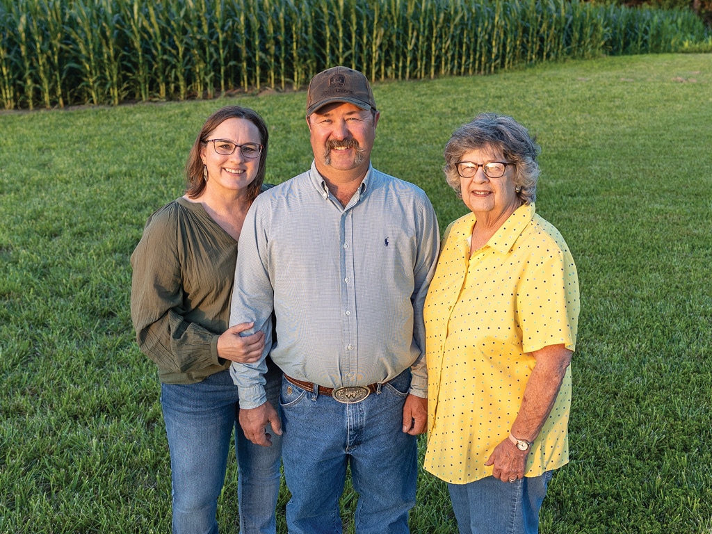 three smiling people standing on a grass lawn