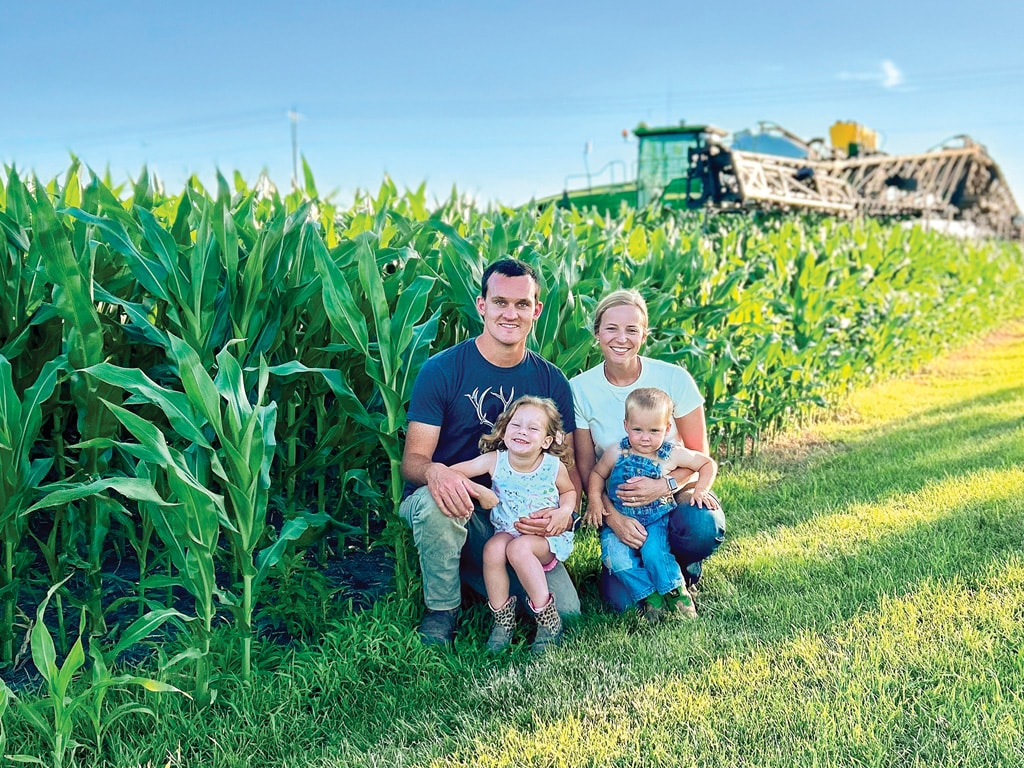 Two adults and two children in front of a crop and tractor