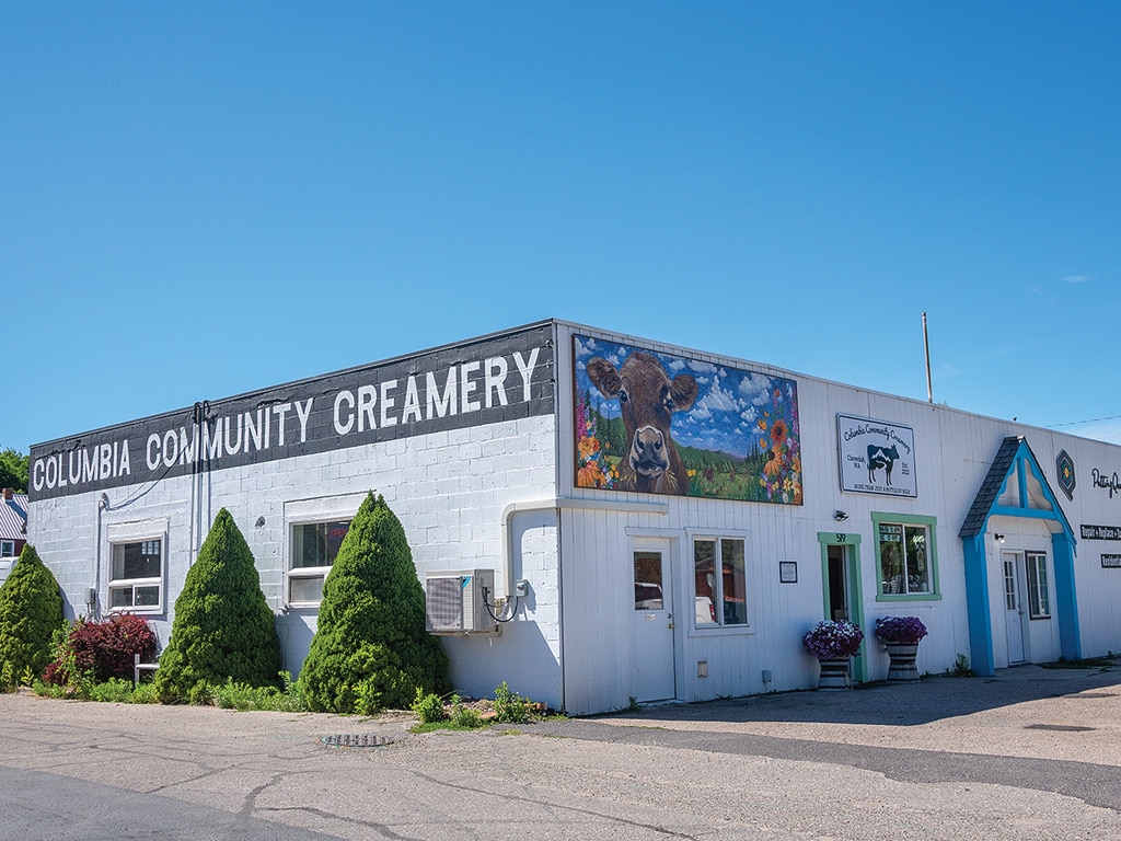 Outside view of a one story white brick building with Columbia Community Creamery painted on the side