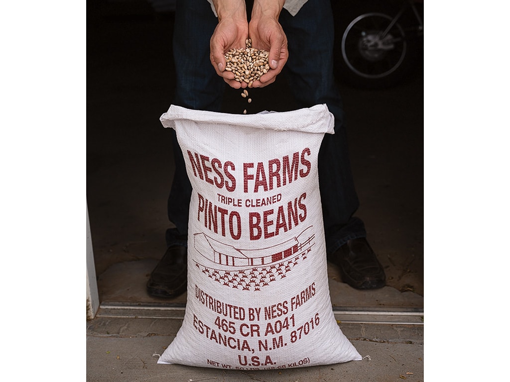 a person's hands pouring pinto beans into a bag labelled NESS FARMS TRIPLE CLEANED PINTO BEANS