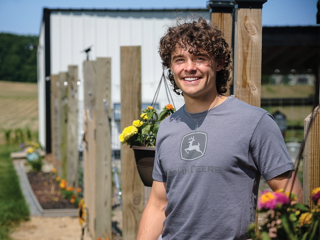 person in a John&nbsp;Deere shirt in front of a flower garden 