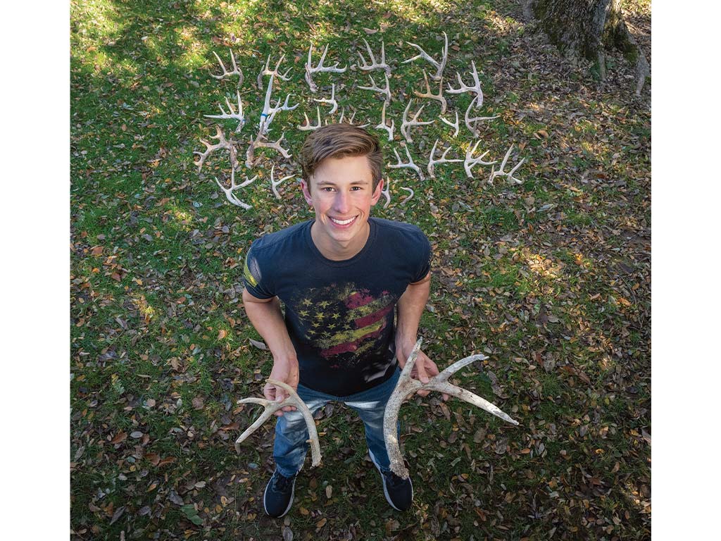 John Bierman smiling holding and surrounded by antlers