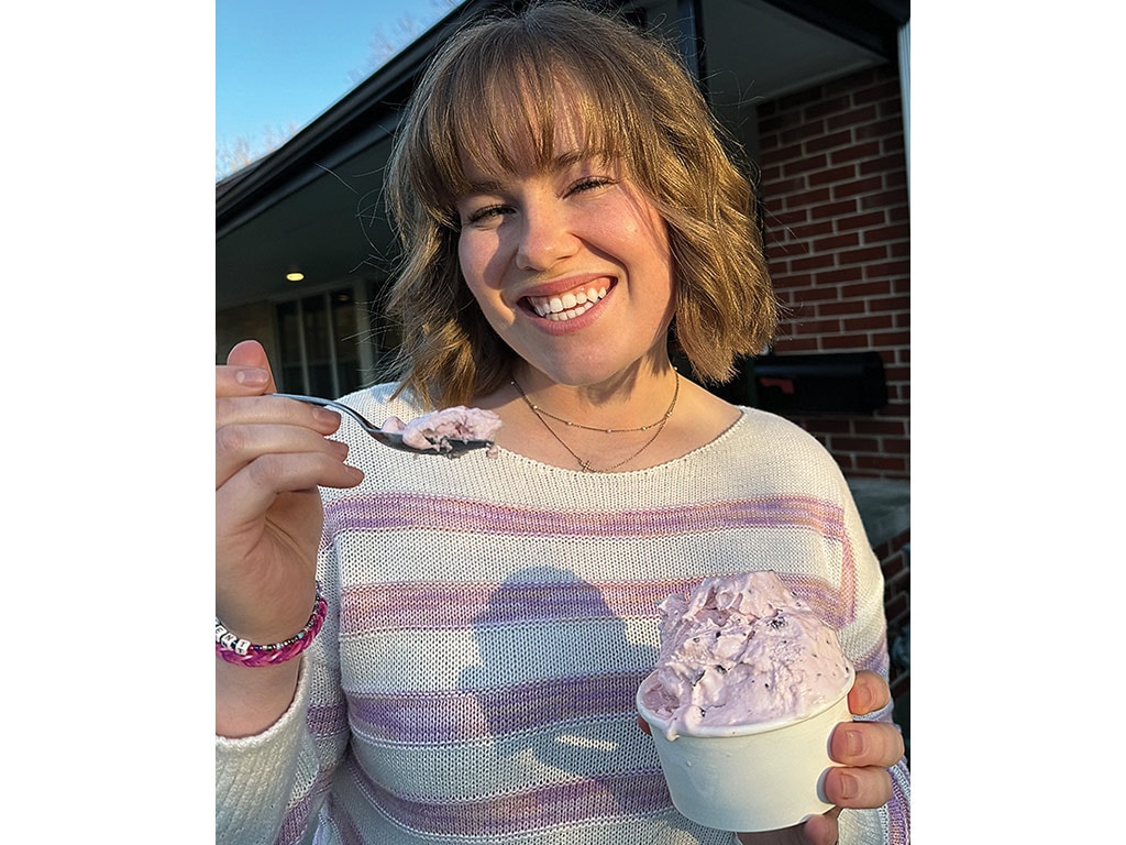 lady smiling holding ice cream cup and a scoop of ice cream in her hand