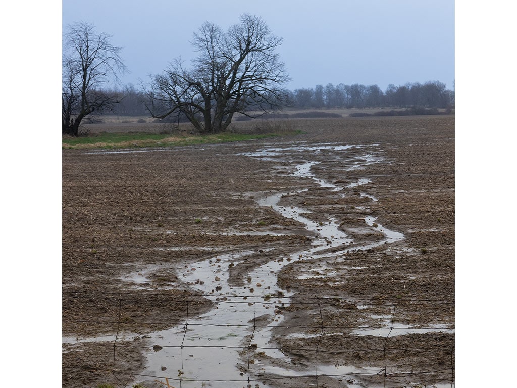 a muddy field full of puddles with an overcast sky