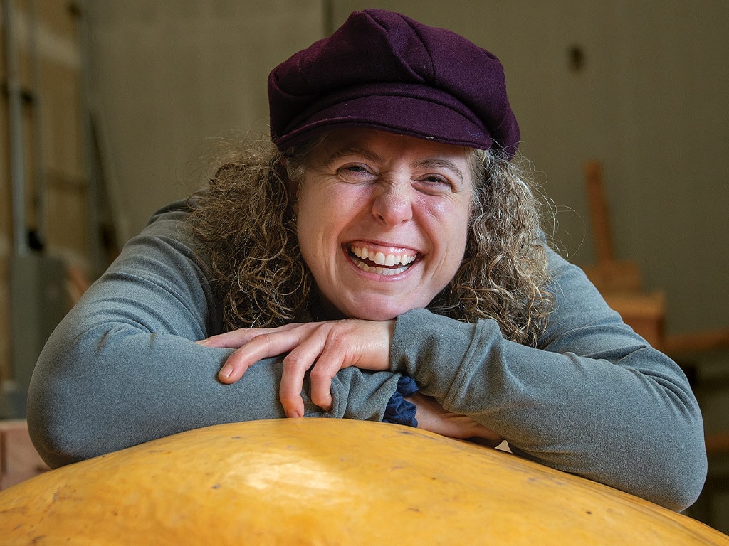 Susan Ashenfelter smiling while resting on her pumpkin