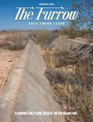 A concrete drainage ditch in the desert full of brown shrubs