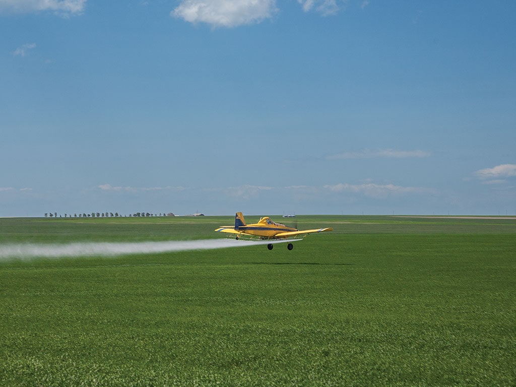 An airplane spraying a large field with herbicides