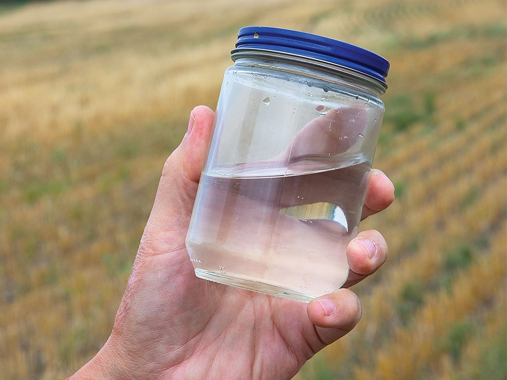 A hand holding a small jar of water with a blue cap.