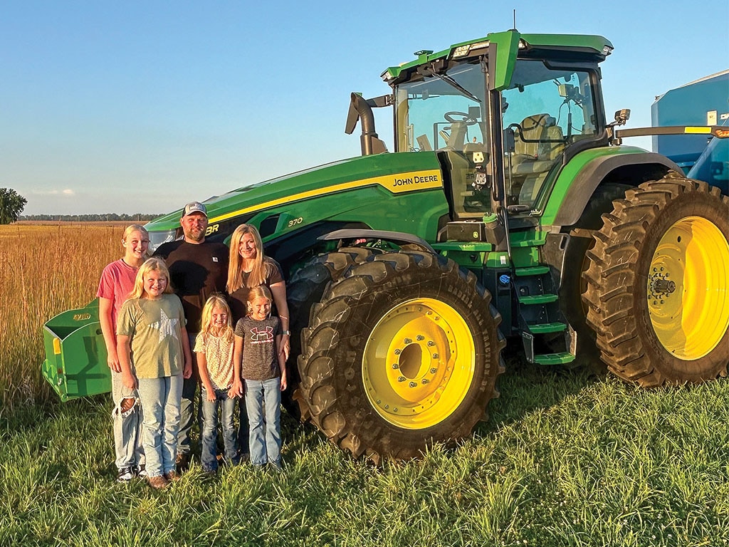 A group standing in front of a green John Deere tractor in a field.