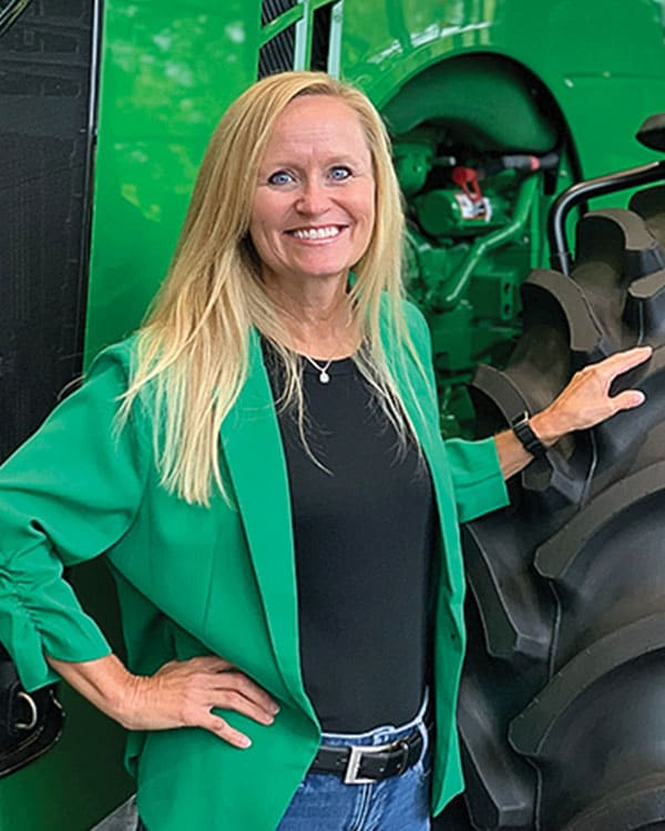 woman in green jacket standing in front of a John Deere tractor