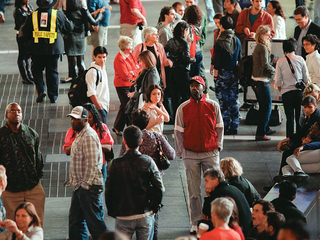 Crowded public area with people walking and sitting, some in conversation.