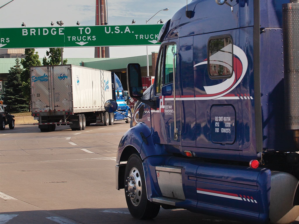 Trucks at a border checkpoint with a sign reading "BRIDGE TO U.S.A. TRUCKS".