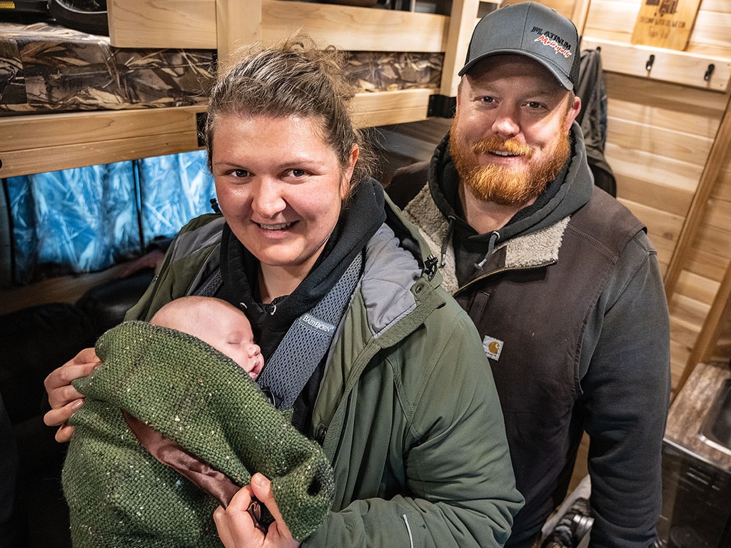 couple inside a wooden cabin, lady holding a bundled child.